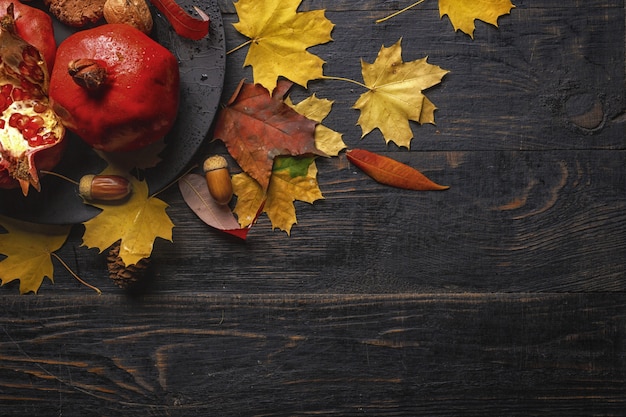 Composición de otoño. Granada con nueces, especias y hojas secas sobre una mesa de madera oscura. Vista superior.