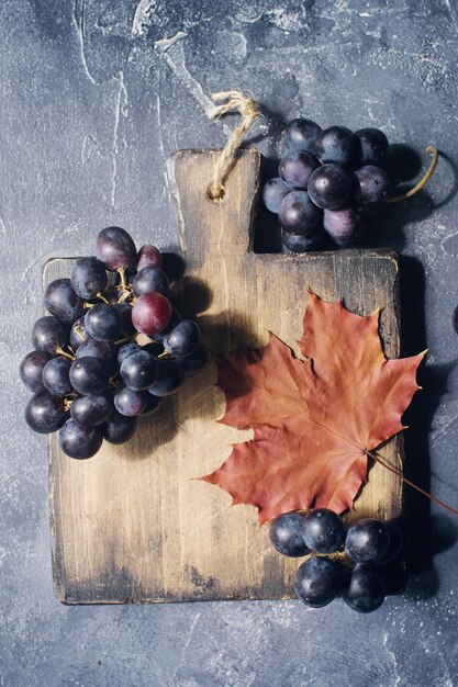 Composición de otoño con hojas de marple de tablero de madera de corte recién cosechadas conos de uvas maduras y nueces en la mesa de piedra oscura Concepto acogedor de otoño