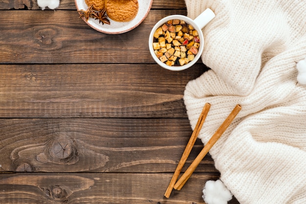 Composición de otoño o invierno. Taza de té de hierbas, suéter blanco de moda femenina, palitos de canela, algodón sobre fondo de madera