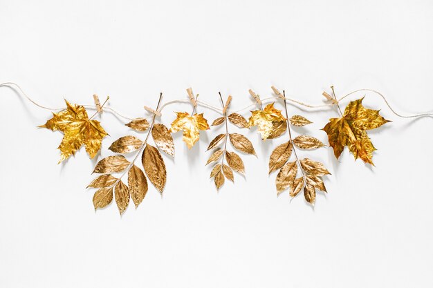 Foto composición de otoño. pinzas para la ropa en la cuerda con hojas otoñales doradas sobre un fondo blanco.