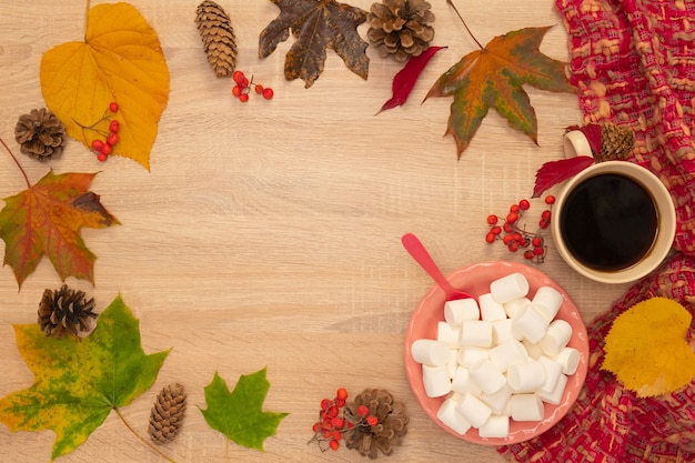 Composición de otoño con una taza de café, malvaviscos y hojas. Disparo desde arriba sobre un fondo de madera. Lugar para su texto.