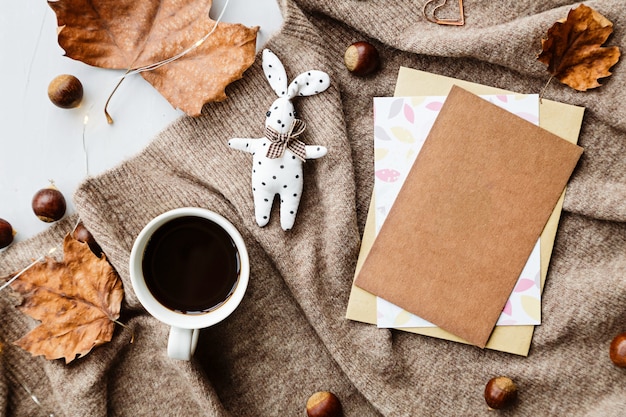 Composición de otoño. Taza de café, manta, hojas de otoño, papel en marrón