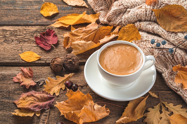 Composición de otoño con una taza de café, un suéter y hojas sobre un fondo de madera marrón