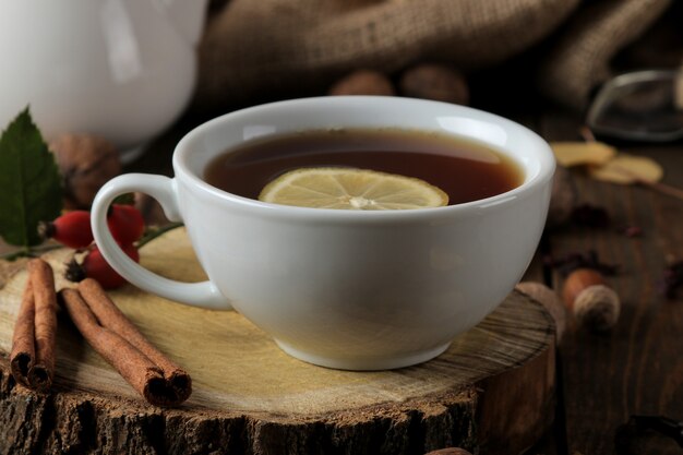 Composición de otoño con té caliente en un soporte de madera, canela, rosa de perro, nueces en una mesa de madera marrón