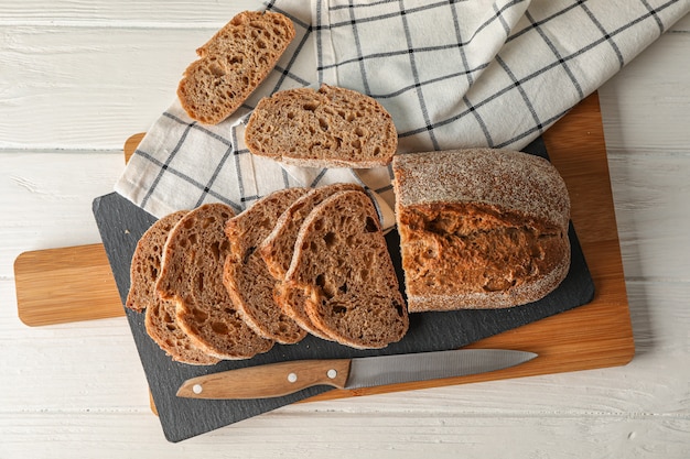 Composición con pan, cuchillo, toalla de cocina y tabla de cortar en espacio de madera blanca, vista superior y espacio para texto