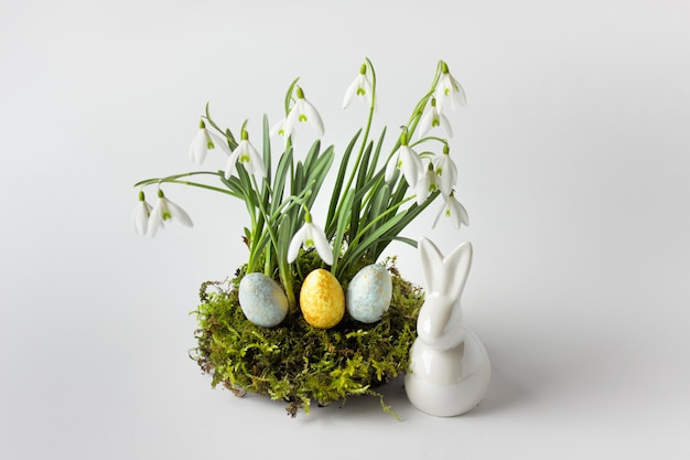 Composición de Pascua con conejito de porcelana blanca y campanillas sobre musgo