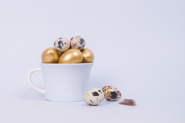 Composición de Pascua de huevos de codorniz y decorativos dorados en taza de porcelana sobre un azul