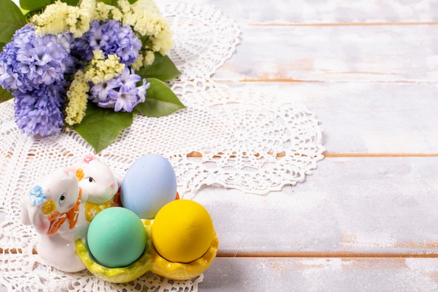 Composición de pascua con huevos multicolores en un standrabbit de cerámica y un ramo de primavera con púrpura