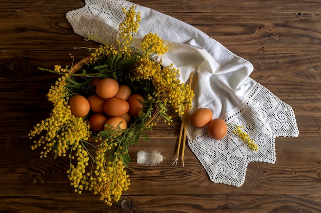 La composición de pascua Huevos un ramo de mimosa amarilla y velas de iglesia en el primer plano de la mesa de madera