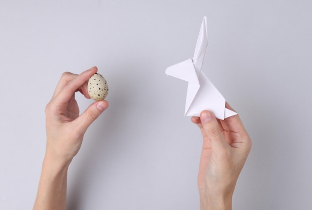 Composición de pascua Manos sostienen huevo de codorniz y conejito de pascua de origami sobre fondo gris