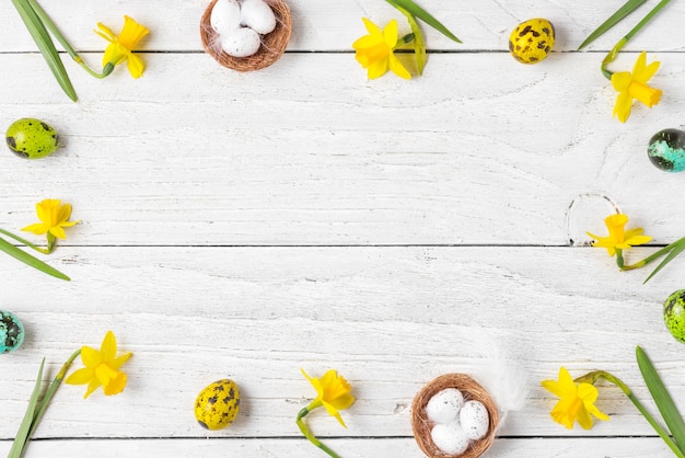 Composición de pascua. Marco hecho de huevos de Pascua y flores de narciso de primavera sobre fondo blanco de madera