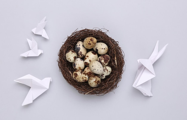 Composición de Pascua Origami Conejito de Pascua y palomas huevos de codorniz en nido sobre fondo gris Vista superior