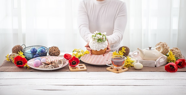 Composición de Pascua con pastel en manos femeninas, té, flores, huevos y detalles de decoración. Concepto de vacaciones familiares de Pascua.