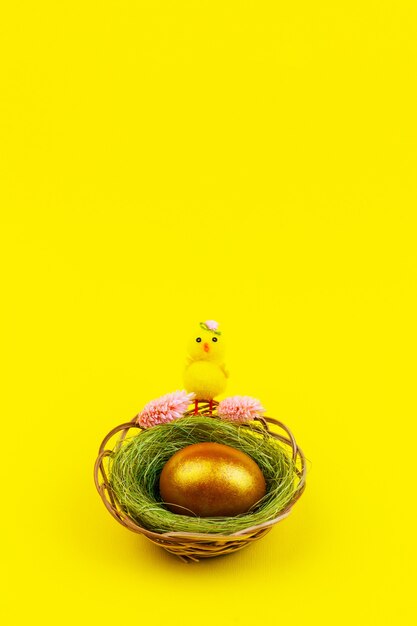 Composición de Pascua con un pollo amarillo y un huevo dorado en un nido sobre un fondo amarillo con un espacio de copia