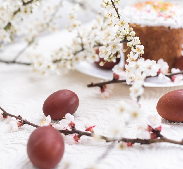 Composición de Pascua. Una rama de albaricoque floreciente, huevos pintados y un pastel de Pascua glaseado decorado con chispas de azúcar.