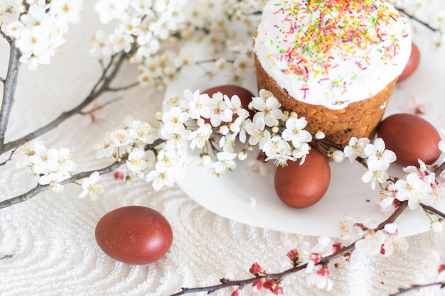 Composición de Pascua. Una rama de albaricoque floreciente, huevos pintados y un pastel de Pascua glaseado decorado con chispas de azúcar