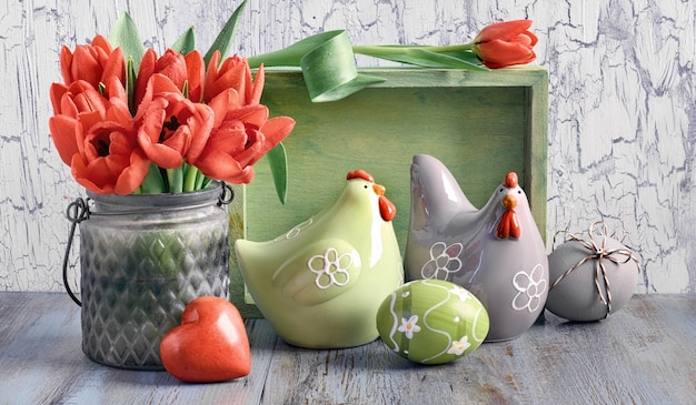 Composición de Pascua con tulipanes rojos, gallinas de cerámica y huevos de Pascua en madera clara