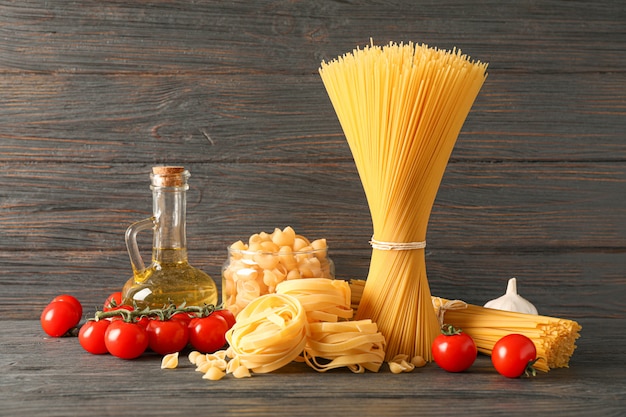 Composición con pasta, aceite de oliva, tomate y ajo en mesa de madera, espacio para texto