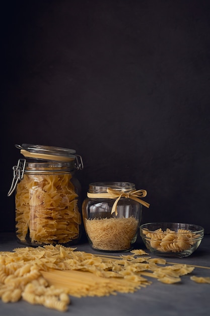 Composición de pasta italiana cruda. Espaguetis, farfalle, fusilli sobre fondo de madera oscura. Fondo de pasta cruda.