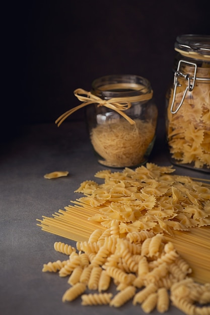 Composición de pasta italiana cruda. Espaguetis, farfalle, fusilli sobre fondo de madera oscura. Fondo de pasta cruda.