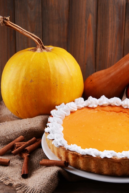 Composición de pastel de calabaza casero en plato y calabazas frescas sobre fondo de madera