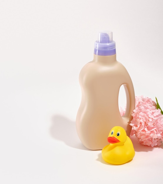 Una composición de un pato de goma amarillo una botella beige de detergente para la ropa y flores rosas Copiar espacio para el texto