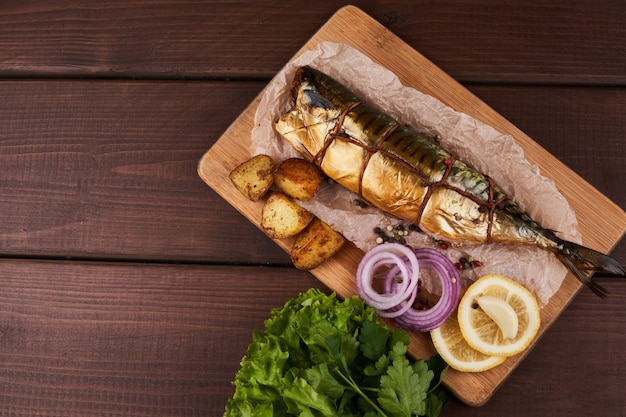 Composición de pescado caballa ahumado con guarnición de patatas cebollas verdes de limón servido en la vista superior de la placa de tablero de madera