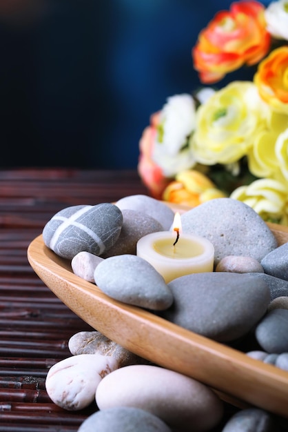 Foto composición con piedras de spa y velas en un tazón de madera cerca de flores sobre fondo brillante