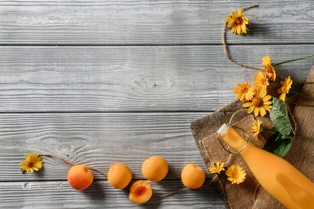 Composición plana con albaricoques, una botella de jugo y flores.