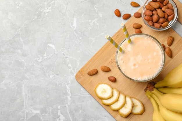 Composición plana de batido de plátano en vidrio y nueces sobre una mesa de mármol gris claro Espacio para texto