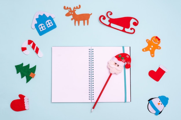 Composición plana con bolígrafo de cuaderno abierto vacío con Santa Claus y juguetes de Navidad manopla pingüino abeto casa del árbol venado trineo calcetín de jengibre