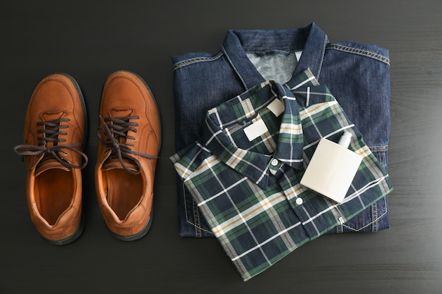 Foto composición plana con chaqueta de mezclilla, camisa, perfume y zapatos en la mesa negra