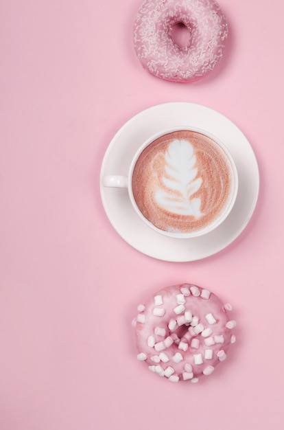 Composición plana con dos donas y una taza de café en rosa