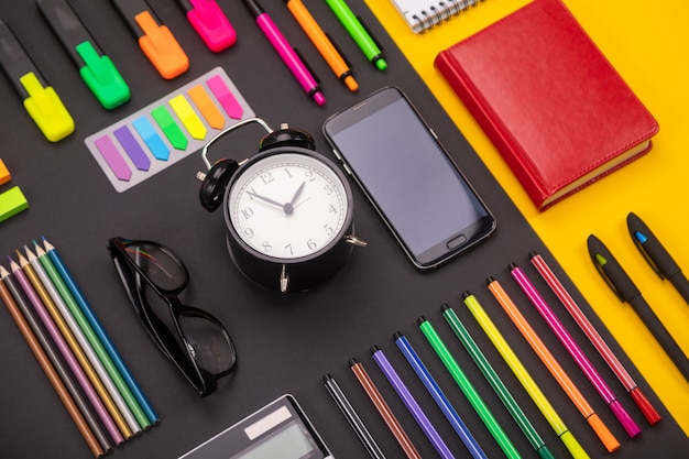Composición plana de escritorio de negocios con reloj despertador, teléfono inteligente, cuaderno, pegatinas y bolígrafos de colores