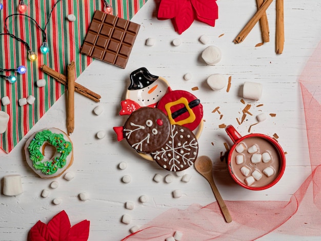 Composición plana con galletas, deliciosa bebida de malvavisco, artículos navideños en mesa blanca.