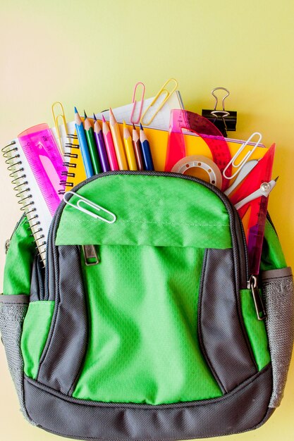 Foto composición plana laico con mochila y papelería escolar sobre fondo amarillo