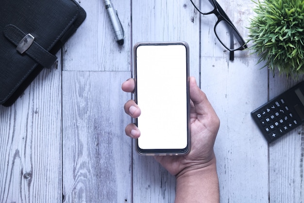 Composición plana de la mano que sostiene el teléfono inteligente sobre fondo blanco