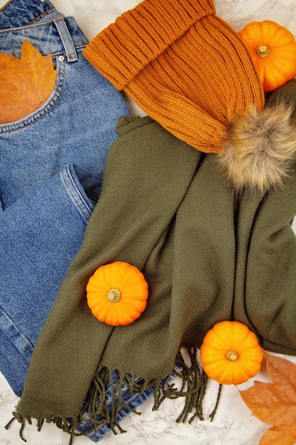 Composición plana de otoño con hojas de otoño, calabazas, jeans y una cálida bufanda de lana y sombrero