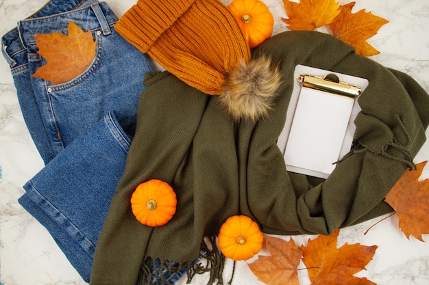 Composición plana de otoño con hojas de otoño, calabazas, jeans y una cálida bufanda de lana y sombrero