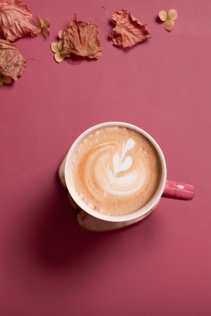 Composición plana de otoño con hojas secas y taza de café con leche sobre fondo de color rosa oscuro creati