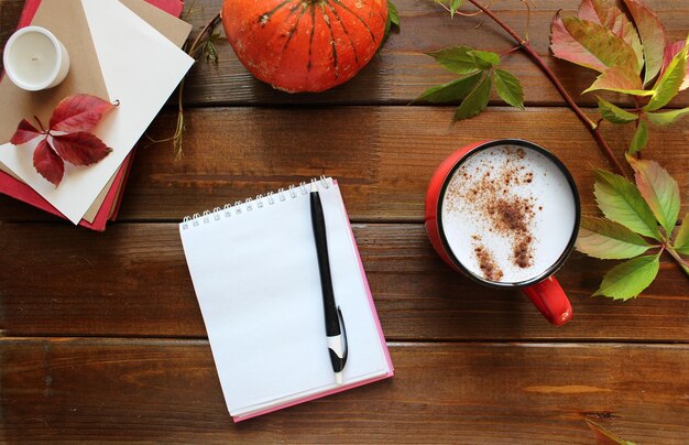 Composición plana de otoño con tarjeta de papel en blanco, sobre de carta, taza de café, bufanda, hojas caídas sobre fondo beige, vista superior de la mesa de escritorio de estilo hygge de otoño