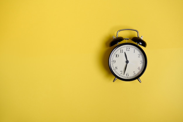 Composición plana con un reloj despertador Vintage negro sobre fondo amarillo con espacio de copia para agregar texto. Regreso a la escuela y conceptos del día del maestro, negocios, organización, gestión del tiempo