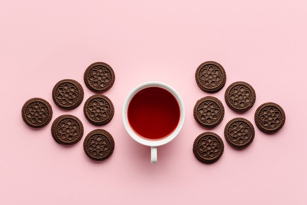 Composición plana con una taza de té de hibisco y galletas de chispas de chocolate aisladas en una pared de color rosa.