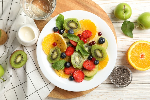 Composición con plato de ensalada de frutas frescas en la mesa de madera blanca, vista superior