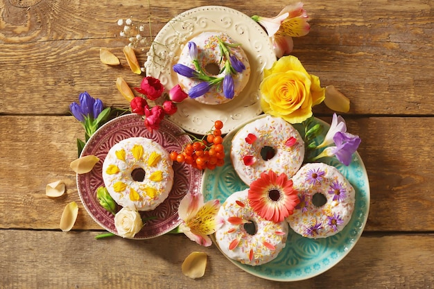 Composición de platos con deliciosos donuts y flores de colores sobre mesa de madera