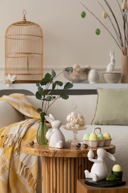 Composición de primavera del interior de la sala de estar con mesa de café redonda sofá beige escultura de conejo de Pascua