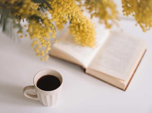 Composición de primavera con un libro de tazas de café y flores de mimosa amarillas sobre un fondo de mesa blanco