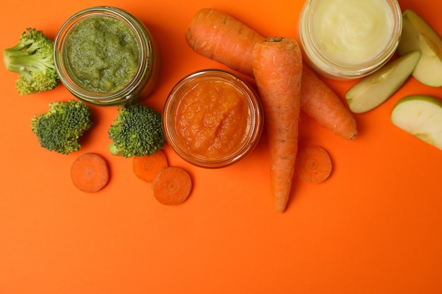 Composición con puré de verduras sobre fondo naranja. Comida para bebé
