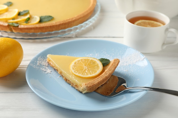 Composición con rodaja de tarta de limón en un plato sobre fondo de madera blanca, de cerca