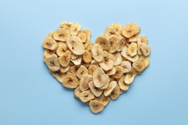 Composición con rodajas de plátano seco dulce sobre un fondo de color. Frutos secos en forma de corazón como merienda saludable